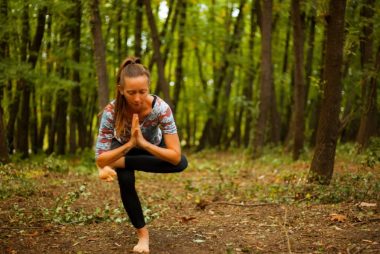 A woman meditates in a yoga pose amidst tranquil woods, focused on relaxation.